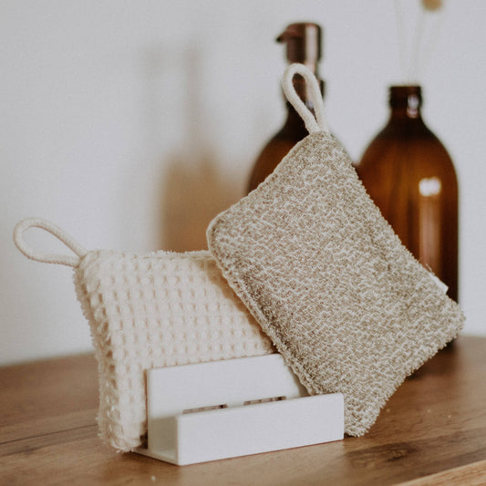 Bio-Küchenschwamm aus Baumwolle auf Holztisch neben Glasflasche