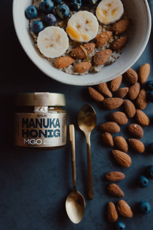 Manuka Honig 250 mit Müsli, Nüssen, Beeren und Frühstück eindekoriert, neben Schale und Löffel, Ansicht von Oben