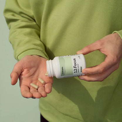Focus supplement dose wird in Hand ausgeschüttet, man sieht einzelne Kapseln vor grünem Hintergrund