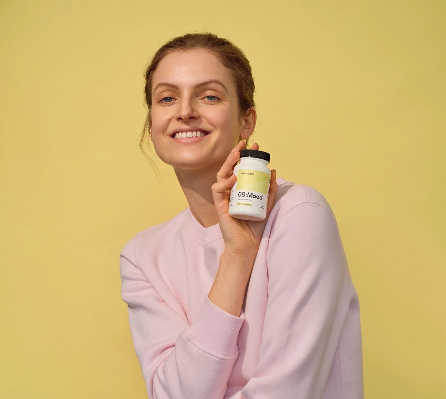 Mood Supplement vegane dose wird vor gelben Hintergrund hoch gehalten 