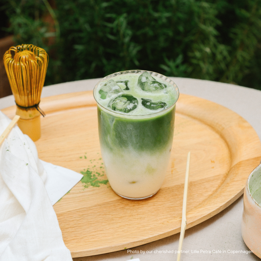 Matcha-Getränk im Glas mit Bambus-Schneebesen und Holztablett